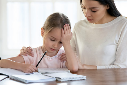 Loving mom sit at desk comfort upset little schoolgirl help with studying or school preparation, caring mom or nanny cheer support unhappy disappointed girl child with learning, education concept