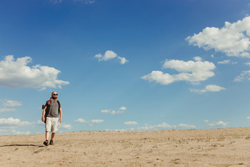Touristic and destination concept. Endurance. Trekking. Powerful man walking through sand dunes in desert