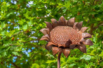 A rusty metal sunflower surrounded by green foliage