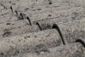 Old roofing tiles made of asbestos and cement. Dangerous and unhealthy roofing, visible old rows of gray tiles on the roof.