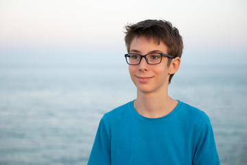 Handsome young happy spectacled boy at beach, sunrise or sunset. Beautiful calm smiling teen boy...