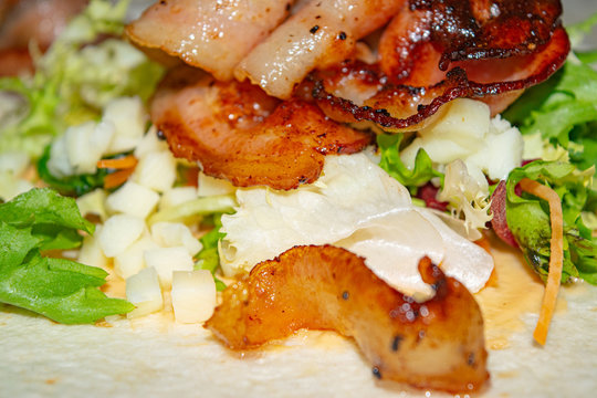 Leafy salad, sliced vegetables, sauce and fried bacon slices on pita bread are the basis for homemade Shawarma. Close up.