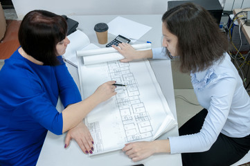 A woman in a blue dress and a girl in the office are working with drawings. The concept of group work