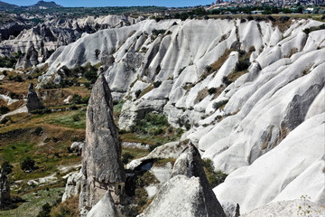 The amazing landscape of Cappadocia. The valley is surrounded by white folded slopes of the mountains. In the foreground is a strange cylindrical rock with a high pointed peak, similar to a mushroom 