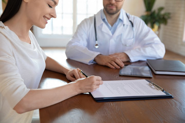 Close up of satisfied woman patient make health insurance agreement with male doctor at consultation, happy female client sign contract document close deal with GP in clinic, healthcare concept