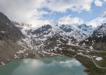glacier lake in the swiss alps during spring with clouds, blue sky and snow taken with a drone