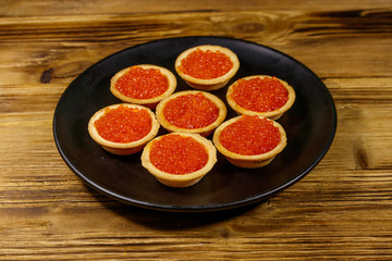 Tartlets with red caviar on a wooden table