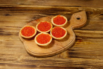 Tartlets with red caviar on a wooden table
