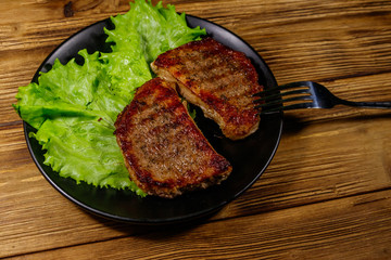 Grilled pork steaks with lettuce leaves on wooden table