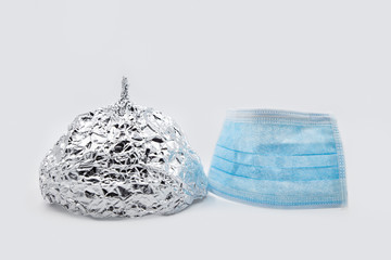 Tin foil hat and surgical mask in front of grey background, conspiracy theory and corona or...