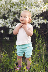 Cute baby girl on a background of white blossoms of an apple tree