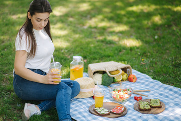 Woman hold disposable cup with orange lemonade on picnic outdoors. Space for text. Vegan picnic concept