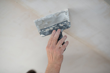 Putty knife in male hand. Hand workю Worker putsty plasterboard ceiling in new appartment....