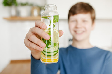 Teenager boy holding glass bottle infused detox water with cucumber, lemon and mint