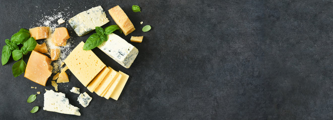 Cheese set: brie, blue cheese, parmesan and basil on a black concrete background. View from above.