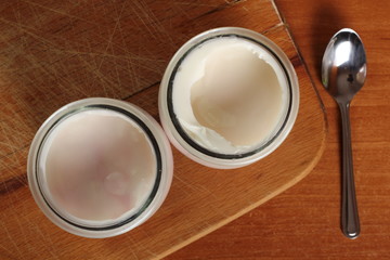Obraz na płótnie Canvas Yogurt in open small glass jar with spoon on wooden cutting board. DIrectly Above.