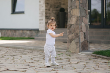 Adorable little girl walk near the house. Beautiful kid spend time in front of the house