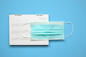 Surgical face mask on 2020 calendar page on blue background Year of Covid-19 Coronavirus prevention concept