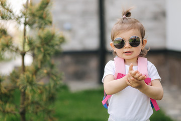 Portrait of Happy litle girl walk in gront of house with backpack. Cute one and half year girl in sunglasses