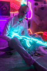 Young man night portrait, lit by neon. Male with green and blue neon gun. Retro games neon light studio. Selective focus.