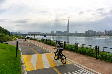 People bike and walk on the Seoul bicycle path along the Han river with Lotte world tower on the background