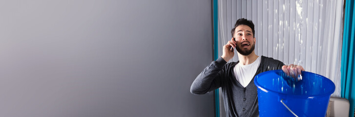 Man Collecting Water In Bucket While Calling Plumber