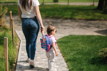 Back view of Mom with her adorable little daughter walk in front of house. Happy family spent time outdoors. Mother and daughter in sunglasses