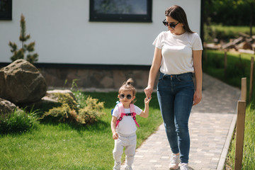 Mom with her adorable little daughter walk in front of house. Happy family spent time outdoors....
