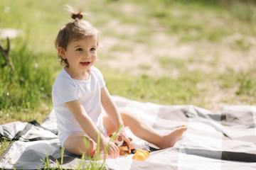 Happy little kid sits outdoors on carpet and play with toy animals. Adorable little girl in white bodysuit