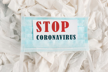 Light blue medical mask on the background of rubber protective white gloves with the inscription. Concept words 'Stop coronavirus'. COVID-19 Pandemic Coronavirus concept.