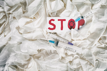 The inscription "Stop" on the background of medical surgical rubber gloves and disposable syringes. Syringe with a needle injected on target on the inscription.