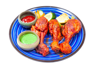 Indian cuisine - portion of Tandoori chicken (spicy chicken legs marinated in yogurt and spices and roasted in tandoor) with sauces on blue ceramic plate isolated on white background