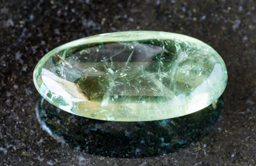 closeup of sample of natural mineral from geological collection - tumbled Prasiolite (green quartz) rock on black granite background from Brazil