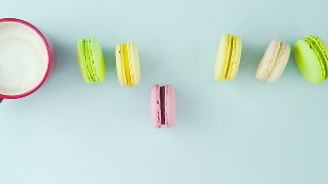 Macaroons or macaron on pastel blue surface with coffee in red cup.