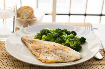 fried fillet of sea bass with garnish of broccoli on black warm stone plate