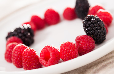 raspberries and blackberries laid out on a white plate in circle