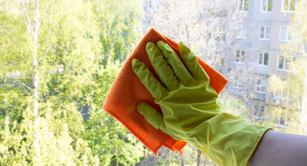 A woman's hand in yellow gloves with an orange rag washes the window . Spring cleaning, home work concept