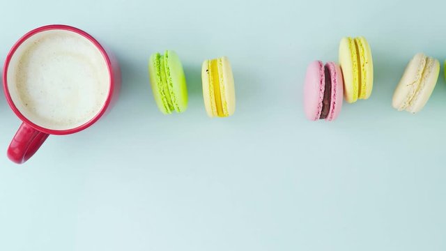 Macaroons or macaron on pastel blue surface with coffee in red cup.