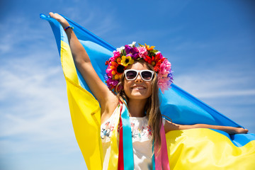 Happy Ukrainian girl carries fluttering blue and yellow flag of Ukraine against blue sky and sea background. Ukrainian flag is a symbol of freedom, liberty, democracy, independence and Europe course