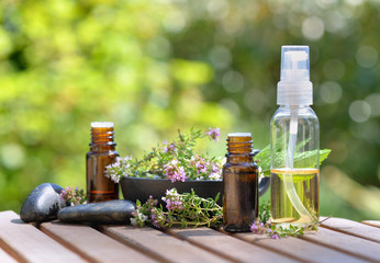 bottles of essential oil and flowers of aromatic herb on a table and on green background
