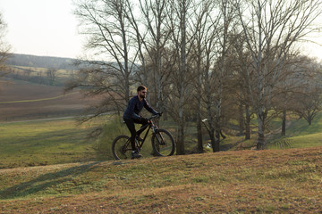 Obraz premium Cyclist in shorts and jersey on a modern carbon hardtail bike with an air suspension fork standing on a cliff against the background of fresh green spring forest