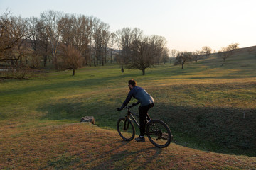 Obraz premium Cyclist in shorts and jersey on a modern carbon hardtail bike with an air suspension fork standing on a cliff against the background of fresh green spring forest