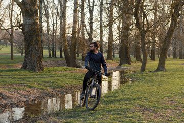 Cyclist in shorts and jersey on a modern carbon hardtail bike with an air suspension fork standing on a cliff against the background of fresh green spring forest