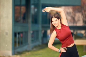 Young sporty woman stretching and exercising in urban park.