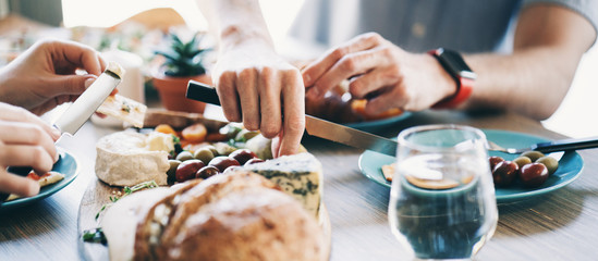 Lots of tasty and delicious food on the table. Dinner at home for romantic couple. Close-up hands with knife. Wide screen panoramic