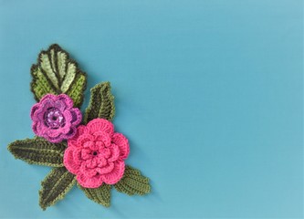 Handmade card design with crocheted flowers and leaves on a blue background.