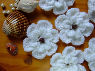 Top view on handmade white crocheted flowers with seashells and pearls on yellow wooden background