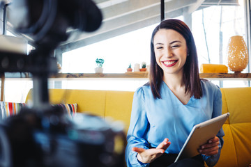 Smiling woman blogger hosting and recording her video show and streaming it to the internet and...
