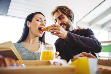 Family couple have pizza break for lunch together in the middle of remote working day. Man feeding woman with a slice