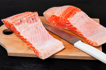 Sliced salmon steak lies on a wooden board with a large knife on a black background